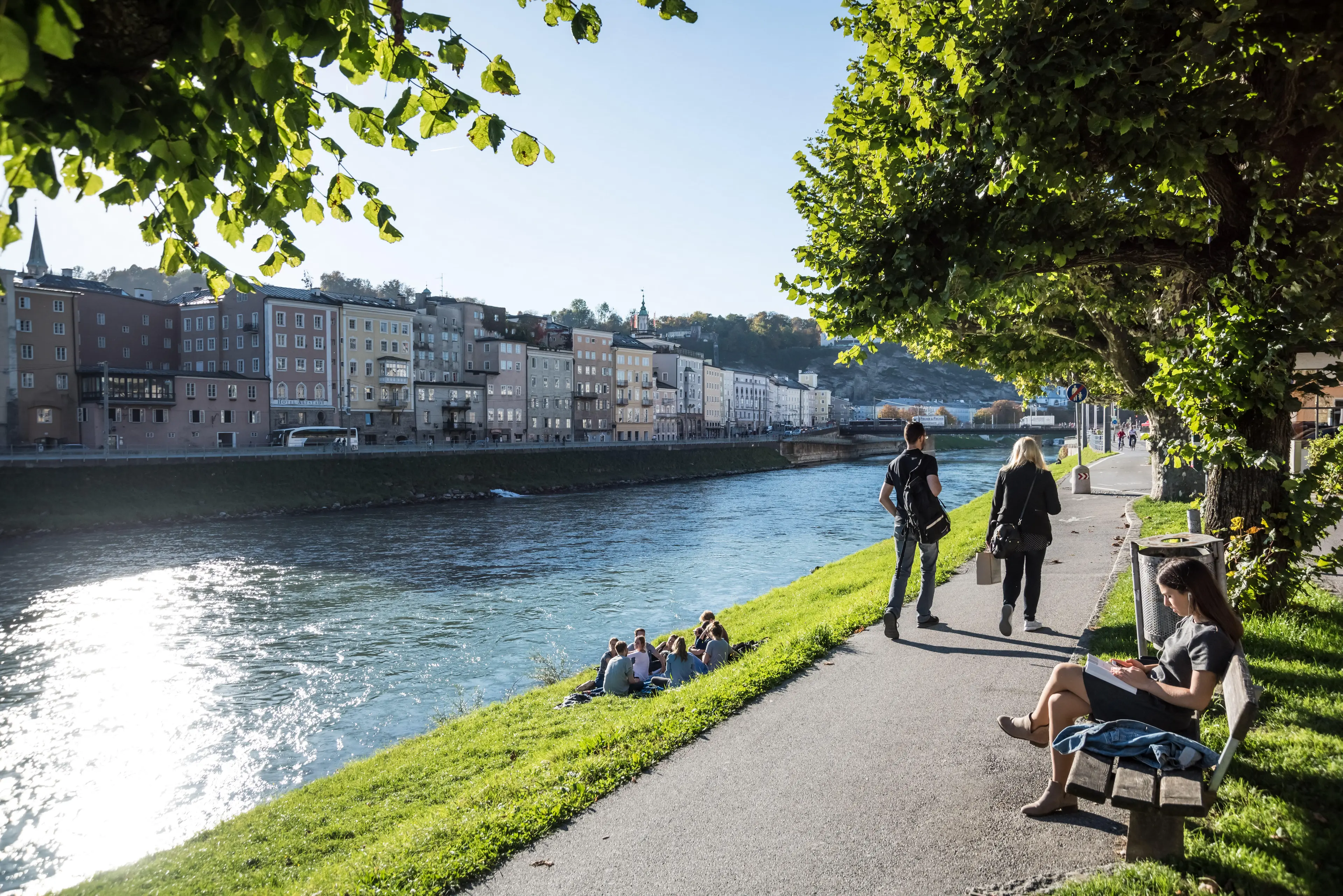 Entspannte Atmosphäre am Salzach-Ufer: Menschen beim Lesen und Erholen im Grünen